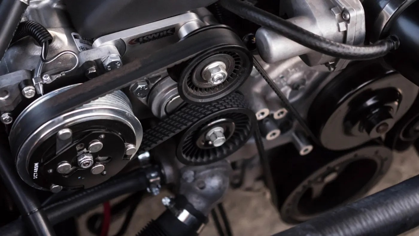 Technician in high-precision bay inspecting serpentine belt assembly and tensioners