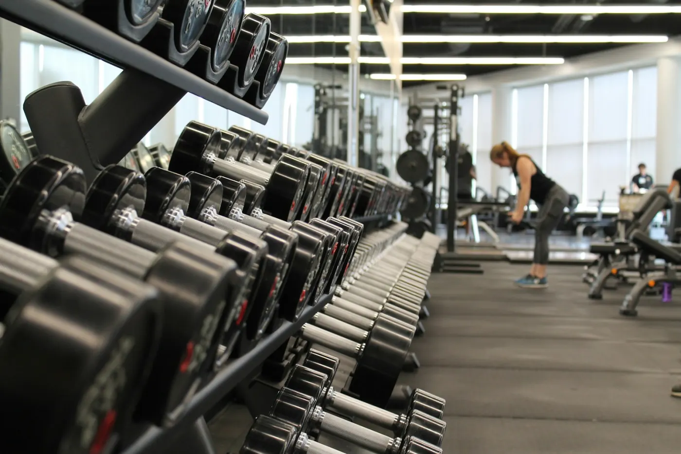 Barbell rack with bumper plates on dense rubber flooring in a natural light warehouse gym